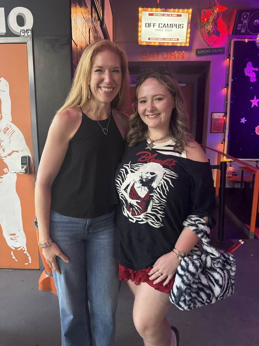 Two women smiling together inside a music venue near an entryway.