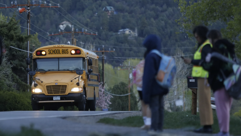 Children wait for their school bus with E.B., a volunteer who arrives at dawn to watch for immigration officials as the kids head off to school in Durango on Monday, April 6, 2026.