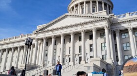 A person speaks into a microphone in front of the Utah capitol building