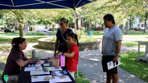A man and woman with their two children speak to a mental health advocate at a book, outside in Frankline Park.