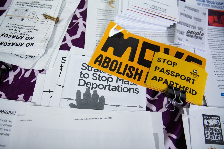 A photo that's looking down on a bunch of white paper and yellow stickers, some of which say "stop mass deportations" and "stop passport apartheid."