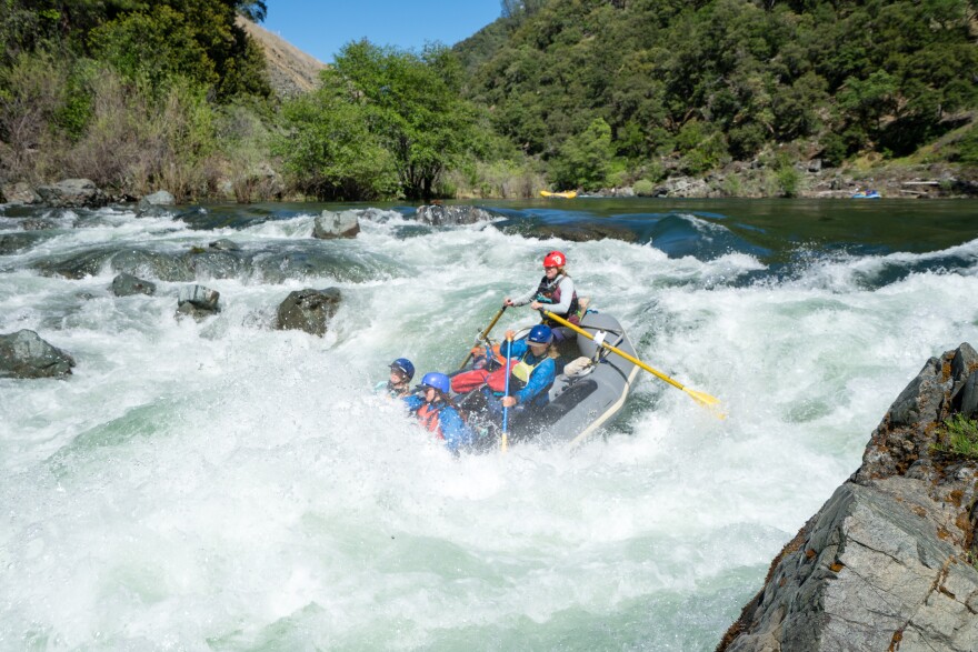 A rafting guide and passengers navigate a whitewater rapid.