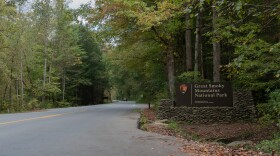 An entrance sign to Great Smoky Mountains National Park on a roadside surrounded by forest.