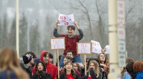 A student sitting on the shoulders of another student holding up a sign in protest.