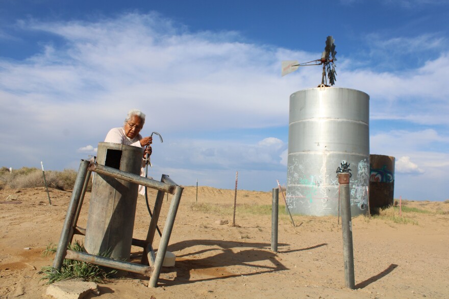 A woman holds a hose next to a metal cylinder on a dusty plain