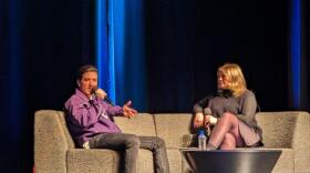 Logan Henderson answers a question, while holding a microphone, seated