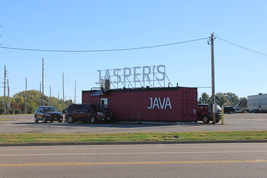 A shipping container converted into a double drive-thru coffee shop has at least three customers in line in their vehicles. 