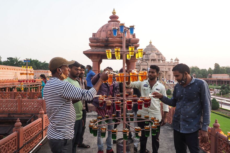 A group of five men light yellow and orange oil lamps outside, with a temple in the distance.