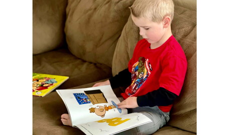 Bjorn Alder, a Lewiston recipient of the Dolly Parton Imagination library, reads cross-legged on a couch.