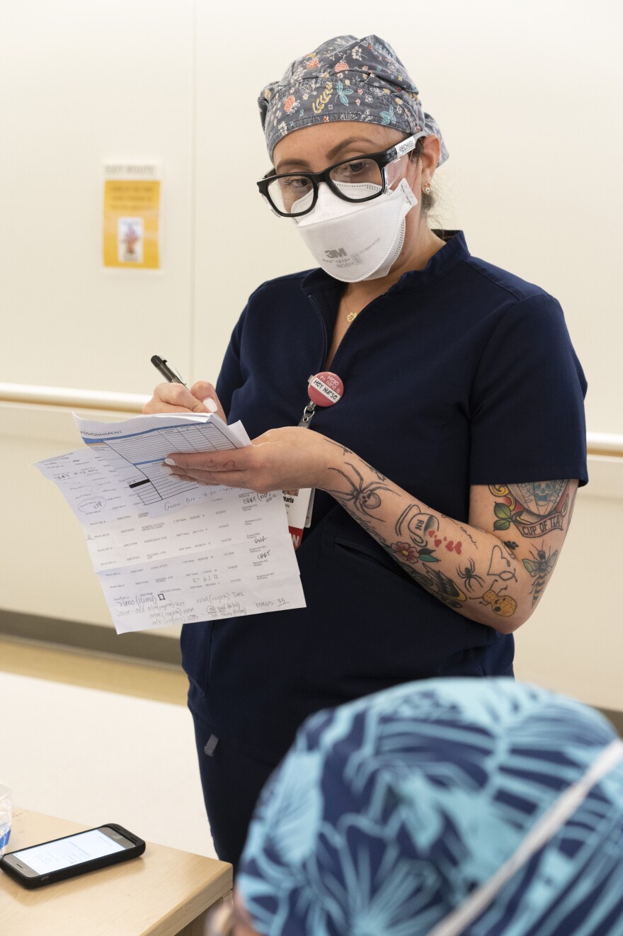 Maria Arechiga takes notes on patients from a nurse who is leaving on lunch break. "I feel like this time around, people are coming in sicker and dying quicker," she says.