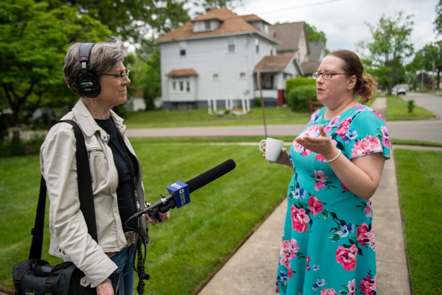 woman in blue floral print dress speaks to woman holding microphone with blue flag that reads "Ideastream Public Media"