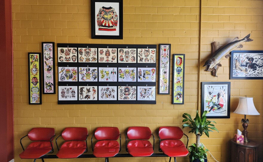 Pictures of tattoos hang on a wall above five red chairs.