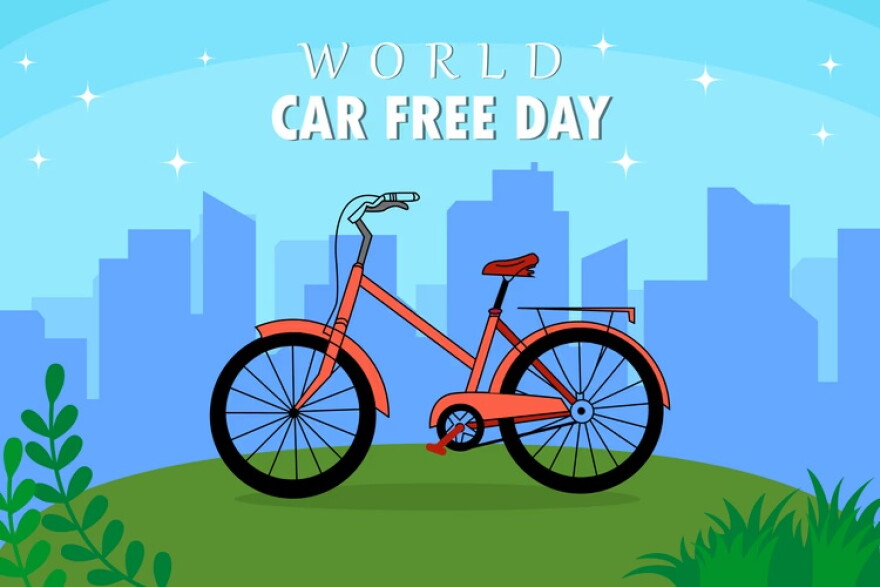 illustration of a bicycle on a green hill in front of a cityscape with the words WORLD CAR FREE DAY over the top 