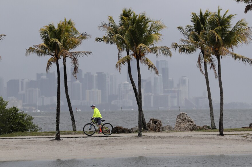 The Miami skyline is shrouded in clouds as a cyclist rides along Biscayne Bay. The National Oceanic and Atmospheric Administration has predicted an unusually active hurricane season this year, with more frequent and intense storms in the Atlantic Ocean. Seas made warmer by climate change are fueling stronger hurricanes, according to the newest research.