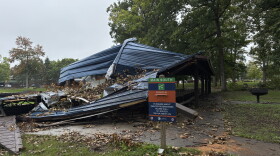 Photo shows a half crushed park pavilion and a park sign.