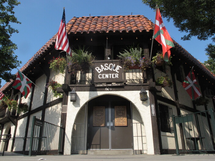 The front of the Basque Center in downtown Boise. It's a white building with black supports and it flies both the American flag and the Basque flag off its top balcony.