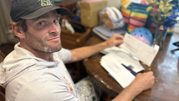 Man sits at table with pile of mail.
