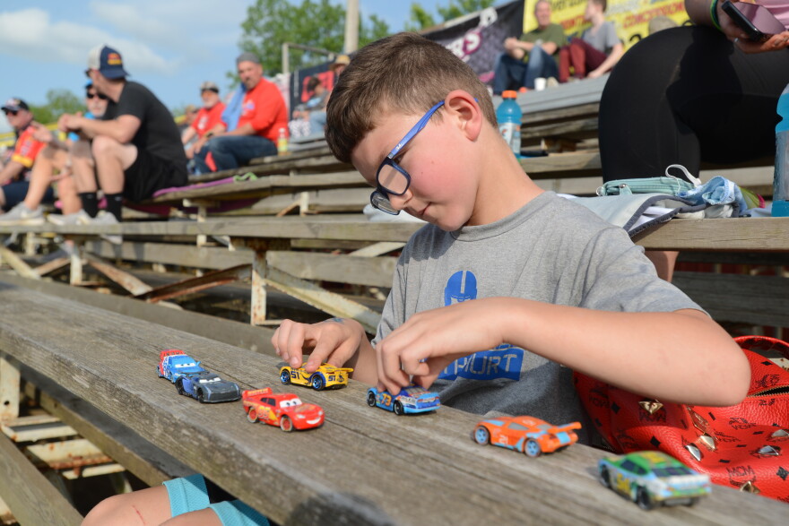 Lucas Snyder, 8, plays with his collection of toy racing cars prior to action getting underway at Valley Speedway in Grain Valley on Saturday. Snyder’s mother, Katie, said her son is a huge fan of the sport and couldn’t deny him an opportunity to see the sport live.