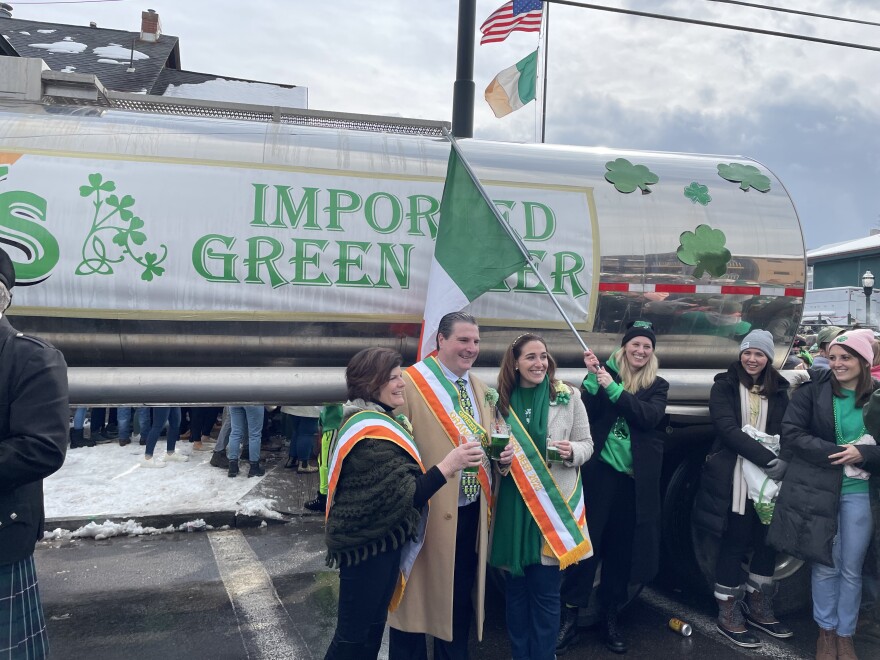 Grand Marshals Mary Kay Ryan (left) and Michael Ryan (center) stand with Miss Green Beer Margaret Cacchione (right) in front of the Coleman's 10,000 gallon tanker truck.