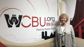 Peoria Area Association of Realtors president Chris Hilton stands next to the mural in the WCBU newsroom.