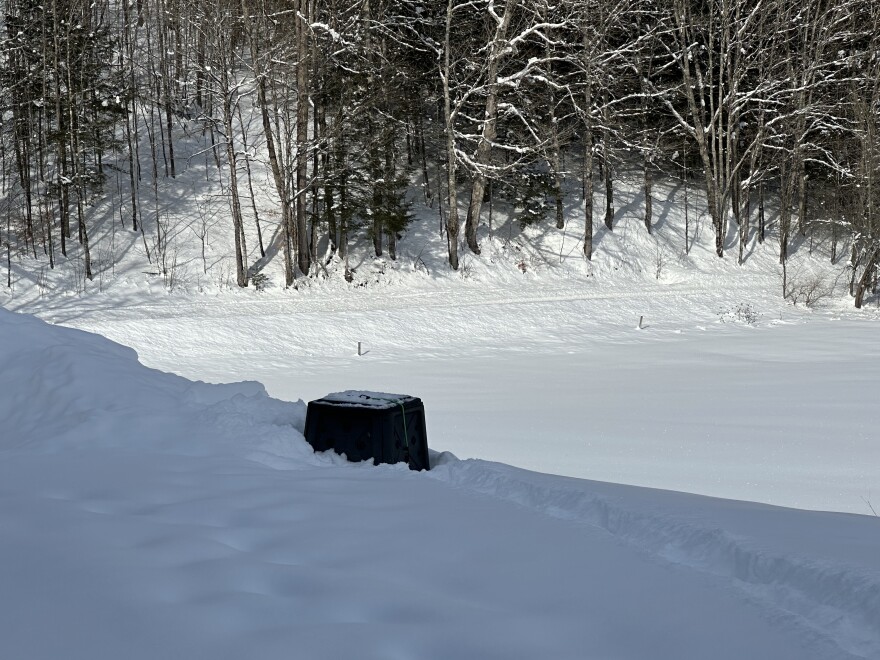compost bin buried in snow, woods and road in distance