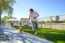 Man runs alongside small dog in dog park. 