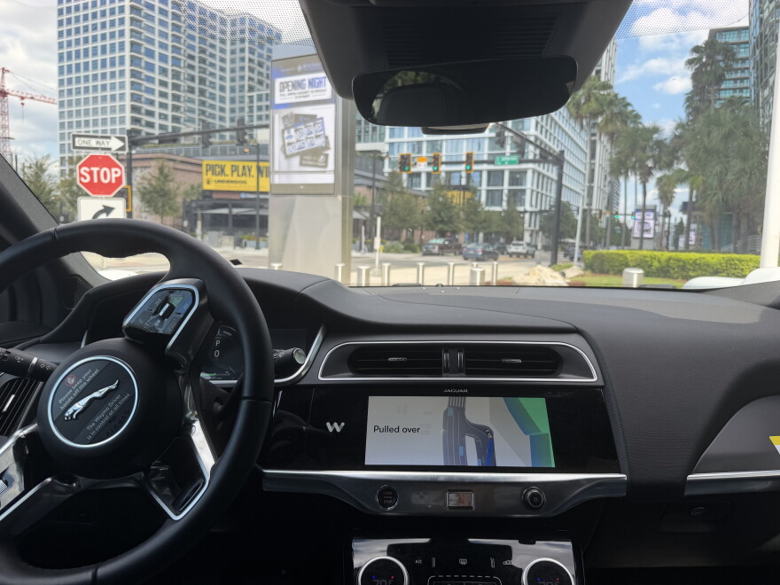 A picture of a car taken from the backseat shows the black interior of a Jaguar, and shows a road map on the center monitor that reads "Pulled over."