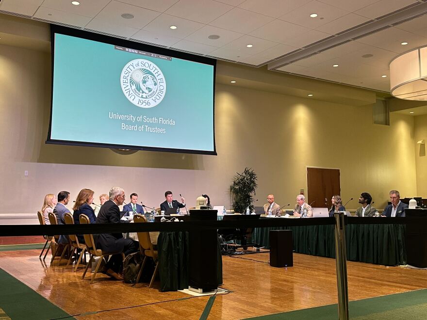 Approximately 15 people sitting at desk during board meeting in conference room. 