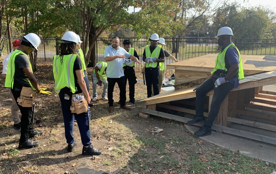 man in blue shirt surrounded by men in bright vests wearing hardhats