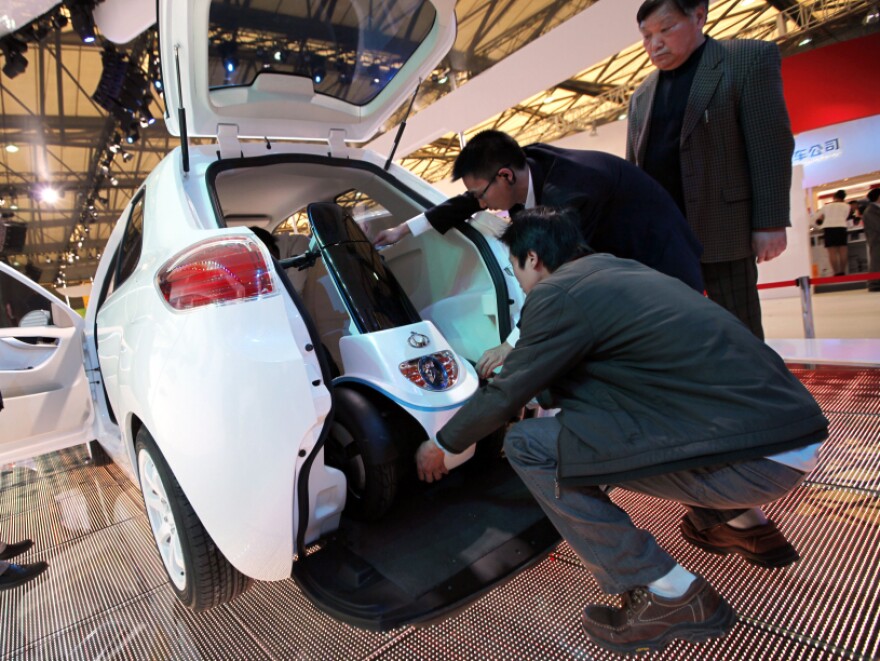 Workers set an electric moped into the back of a McCar, a new Geely's concept car, at the Shanghai International Auto Show on Wednesday, April 20, 2011 in Shanghai.
