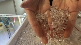 A woman's hand scoops up a tray full of diamond looking stones that are actually Herkimer Diamond quartz.