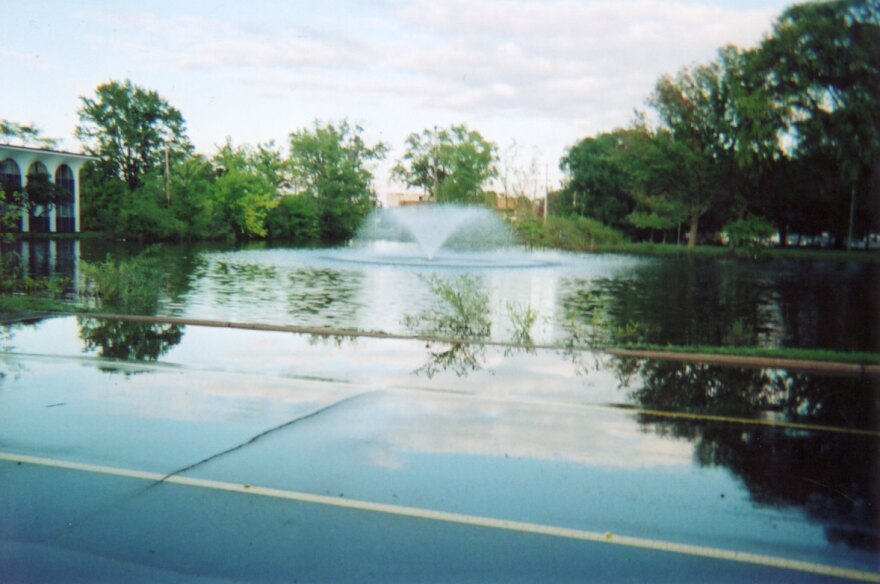 The fountain can be see spraying in a trumpet shape during a flood event in 2008. Crosstown Parkway is underwater. The Forum office building can be seen in the background and is reflected in the water. 