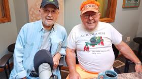 Two men sit at microphones in KAXE's studio. One is wearing a John Deere hat and the other is wearing Allis-Chalmers gear.