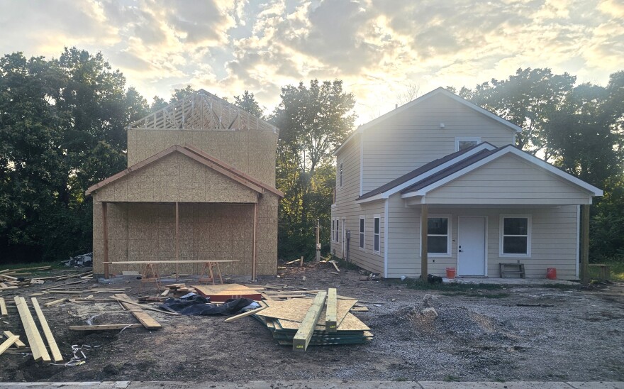 Two houses sit at a construction site. The one on the right is almost finished, while the one on the left still needs exterior paneling and a roof.