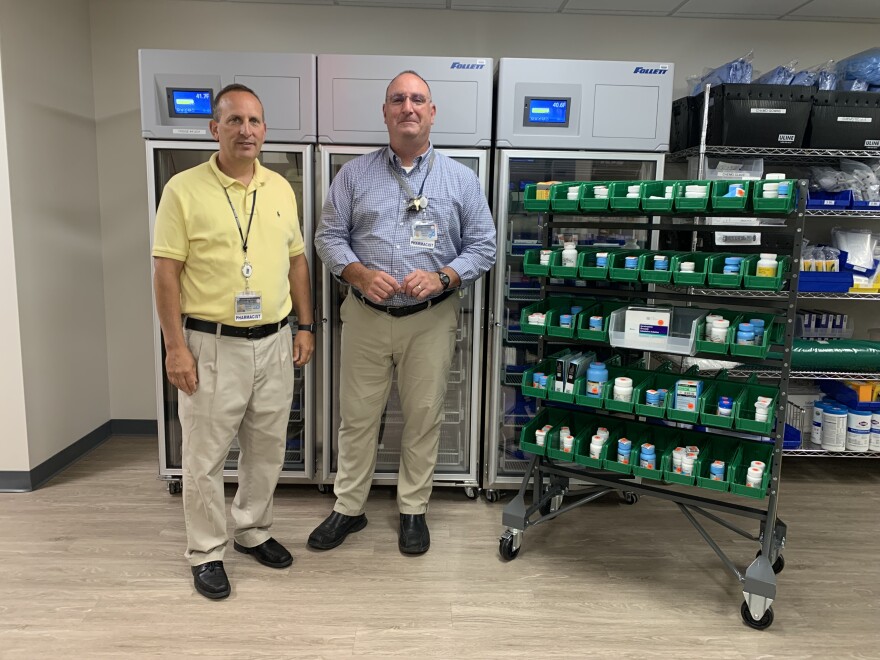 Eric Balotin and David Geloso from Upstate Medical’s “Medications for Hope” pose for a photo alongside storage boxes of medication.