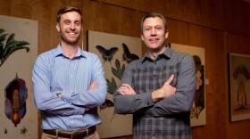 Jordan Teisher and Matthew Albrecht cross their arms in front of plant drawings