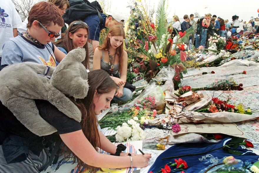 Amber Johnson (left front) writes a note for the Columbine High School shooting victims with friends on April 26, 1999, at the memorial site in Clement Park in Littleton, Colo.
