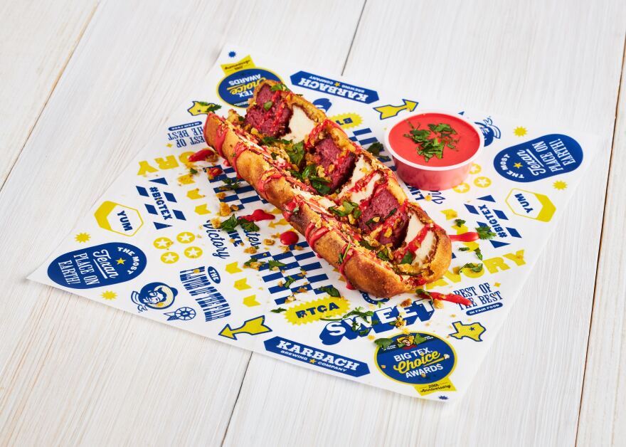 A hot-dog looking food item cut down the middle next to a cup of red sauce, on a State Fair of Texas serving paper.