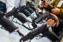 We see hands holding guns that are on display in a store
