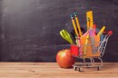 Small shopping cart with school supplies parked in front of a chalkboard 