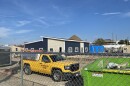 Construction of a building sits behind a fence, nearby is a work truck, a dumpster and other supplies.