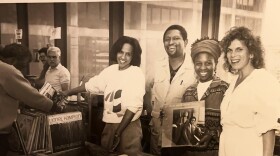 A black-and-white photo of vendors and visitors at the WBGO Record Fair in the 1990s, with people smiling and holding vinyl records at a booth displaying Lionel Hampton records