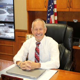  Jose Cubero sitting behind his desk wearing a tie and smiling.