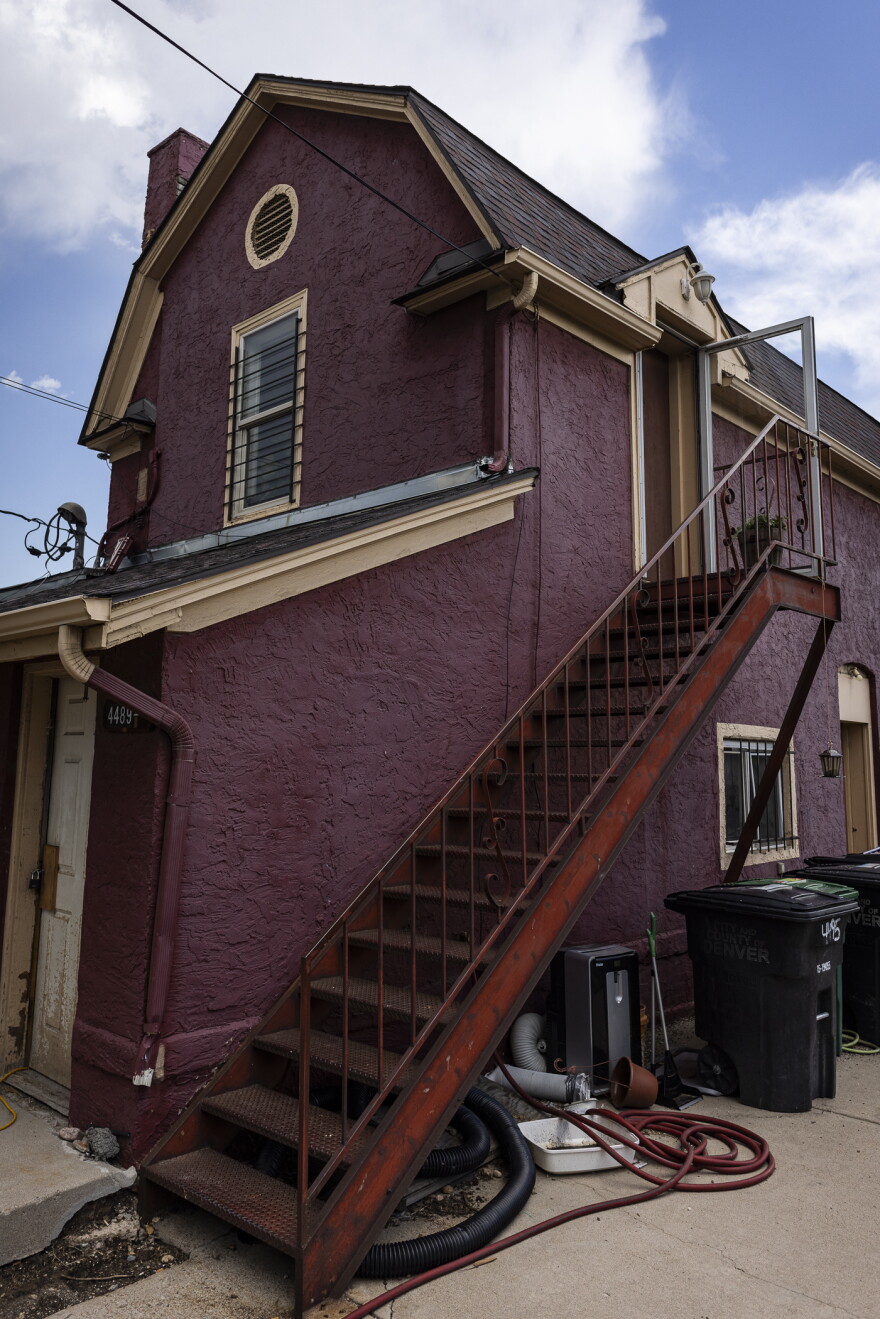 A tall burgundy house stands tall against blue, partially cloudy skies, with a red staircase on the side.