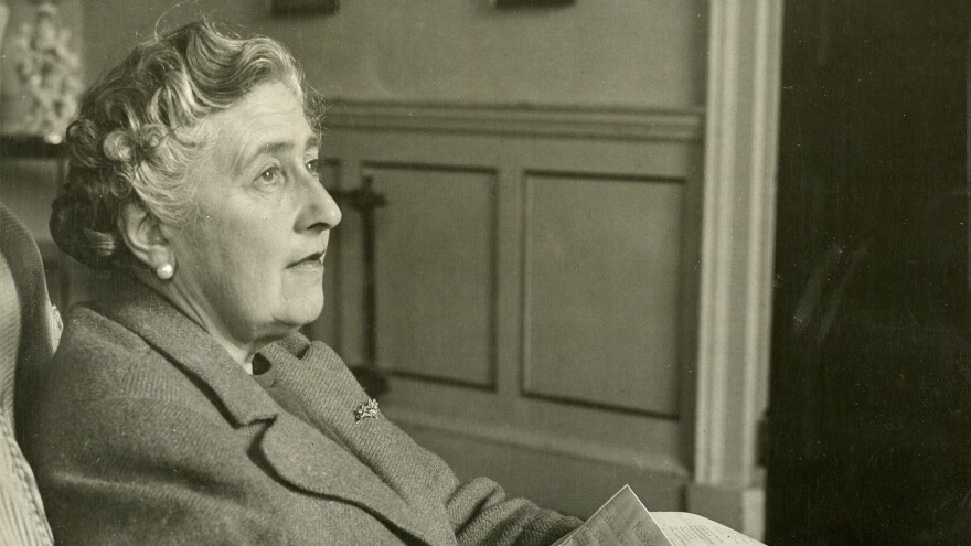 Agatha Christie sitting, looking into distance, with papers in lap