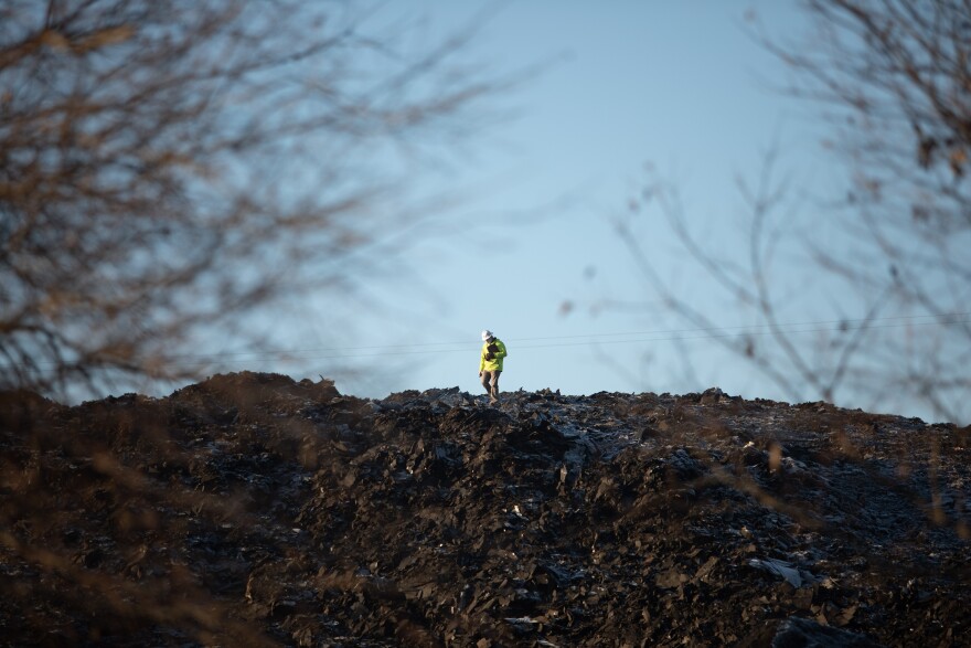 A person wearing construction gear stands on top of the six-story pile of shingles known as Shingle Mountain. They work with Modern Geoscientists, an environmental company that inspects the air quality during the removal process to make sure the air is not harmful to residents.