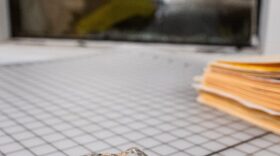 A rock that was thrown through the windows at CJ’s Bail Bonds in Oklahoma City sits on a table inside the business with a shattered and boarded up window in the background. A large area inside the business is closed off until the damage is repaired.