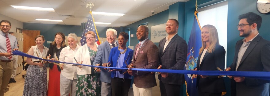 State officials smile while holding a long blue ribbon to mark the opening of the Buffalo computer-based testing center