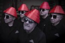 Five men wearing sunglasses, black shirts and red hats in the shape of a cone, tapered toward the top