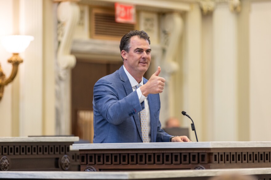 Oklahoma Gov. Kevin Stitt is walking up to a podium to talk to reporters during a press conference.